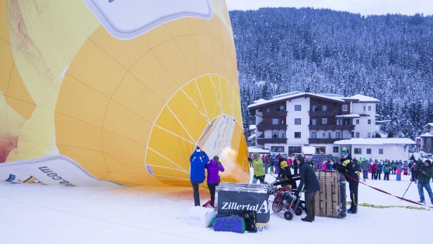 Ein gelber Heißluftballon wird auf einem schneebedeckten Feld vorbereitet.