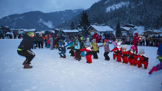 Eine Gruppe Kinder macht unter Anleitung eines Trainers Übungen im Schnee.