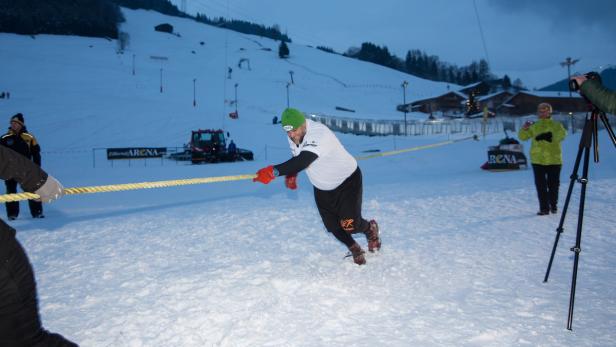 Ein Mann zieht an einem Seil im Schnee, während andere zusehen und fotografieren.