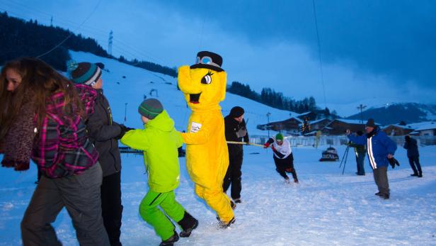 Eine Gruppe von Menschen und ein gelbes Elefanten-Maskottchen ziehen ein Seil im Schnee.