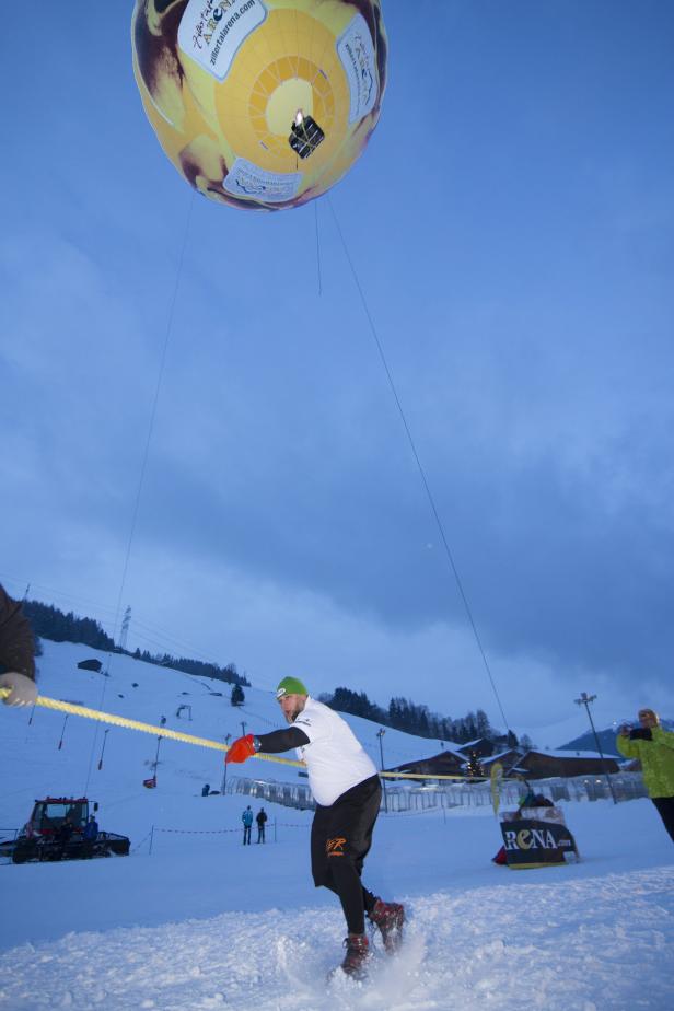 Ein Mann wird von einem Heißluftballon über eine verschneite Landschaft gezogen.