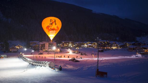 Ein beleuchteter Heißluftballon über einem verschneiten Dorf bei Nacht.
