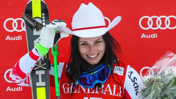 Eine Skirennläuferin mit einem Cowboyhut posiert vor einem roten Hintergrund mit Audi-Logos.