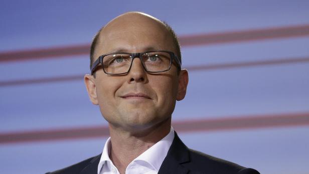 Ein Mann mit Brille und Anzug vor einem blauen Hintergrund.