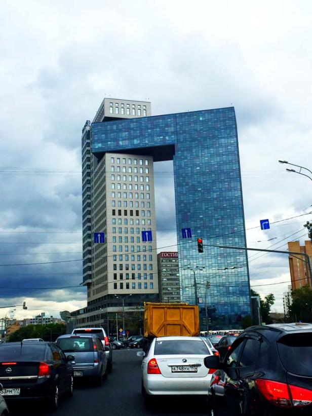 Ein modernes Bürogebäude mit einem großen Durchgang in der Mitte, gesehen von einer belebten Straße.
