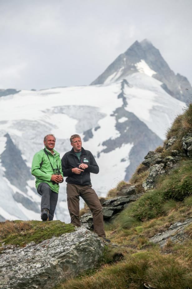 Zwei Männer stehen in den Bergen und betrachten die Landschaft.