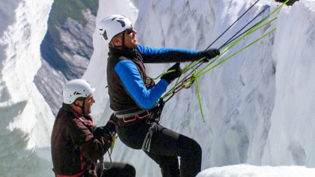 Zwei Männer klettern mit Seilen und Helmen eine Eiswand hoch.