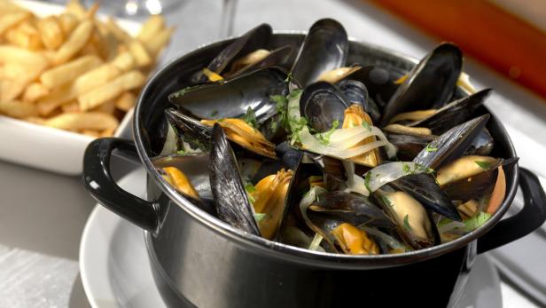 Ein Topf mit Miesmuscheln und Zwiebeln, serviert mit Pommes Frites.