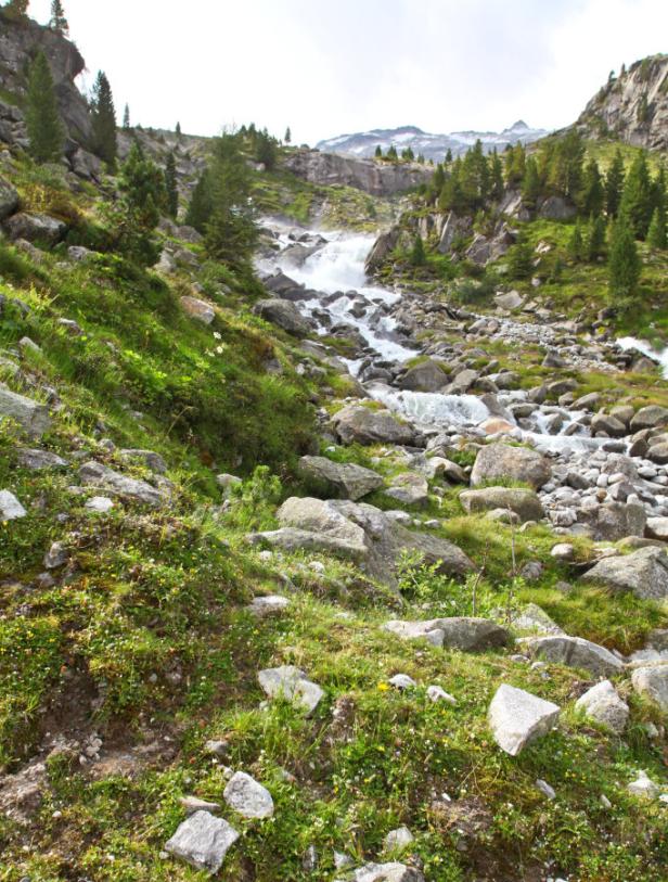 Ein Wasserfall fließt über Felsen in einer grünen Berglandschaft.