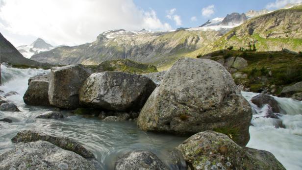 Ein Gebirgsbach fließt über Felsen vor einer Bergkulisse.