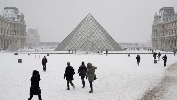 Schneefall auf dem Vorplatz des Louvre in Paris mit der Glaspyramide im Zentrum.
