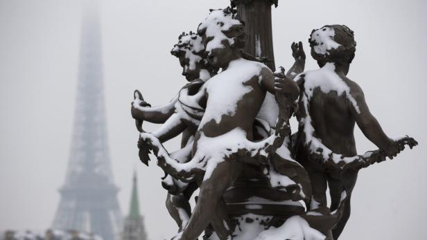 Eine von Schnee bedeckte Figurengruppe vor dem verschneiten Eiffelturm in Paris.