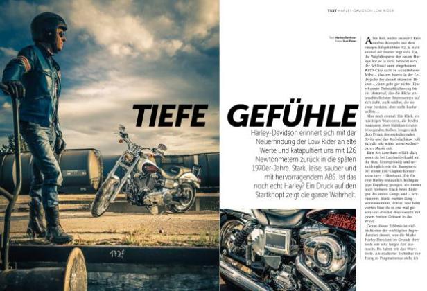 Ein Mann mit Helm steht neben einer Harley-Davidson Low Rider vor Industrieanlagen.