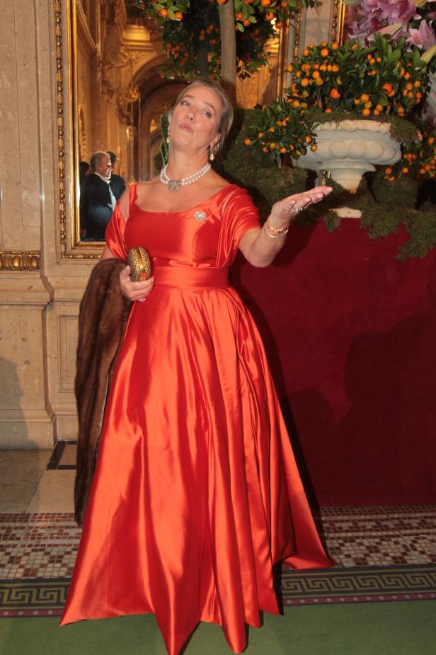 Eine Frau in einem roten Ballkleid posiert in einem eleganten Raum.