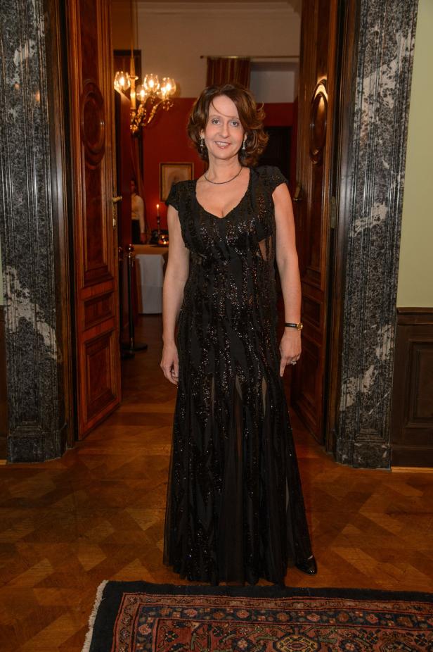 Eine Frau in einem schwarzen Abendkleid steht in einem eleganten Raum.