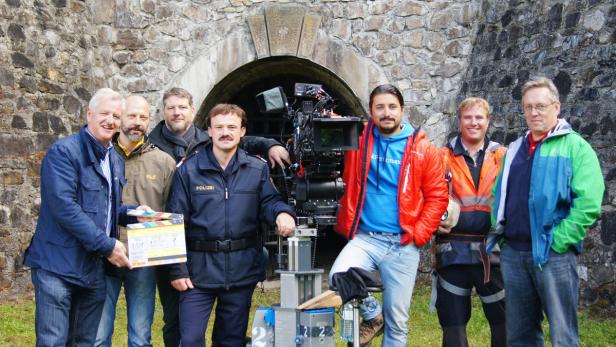 Eine Filmcrew mit Kamera und Klappe vor einer Steinmauer.