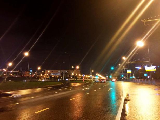 Nachts auf einer nassen Straße mit hellen Straßenlaternen und Autos im Hintergrund.