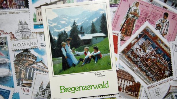 Eine Postkarte mit einer Szene aus dem Bregenzerwald, auf Briefmarken liegend.