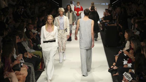 Models präsentieren Mode auf einem Laufsteg vor einem Publikum.
