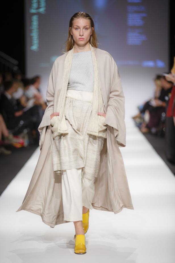 Eine Frau präsentiert ein beiges Ensemble und gelbe Schuhe auf einem Laufsteg.