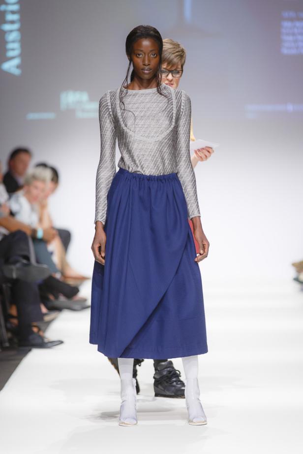 Eine Frau präsentiert ein Outfit mit blauem Rock und silbernem Oberteil auf dem Laufsteg.