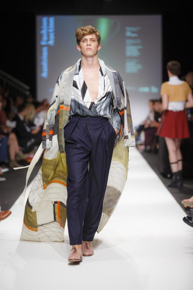 Ein Mann präsentiert ein Outfit mit gemustertem Mantel auf einem Laufsteg.