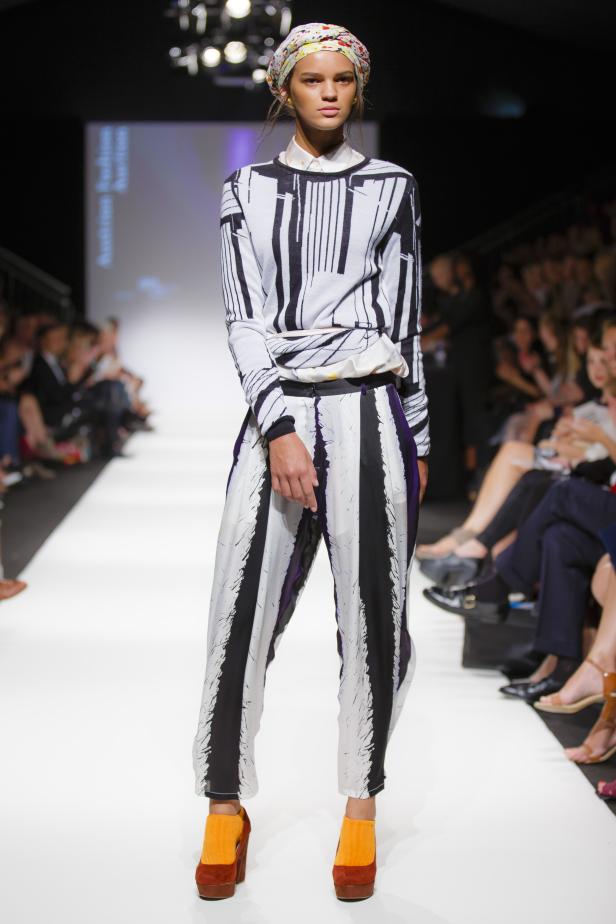Eine Frau präsentiert ein schwarz-weißes Hosen- und Oberteil-Set auf einem Laufsteg.