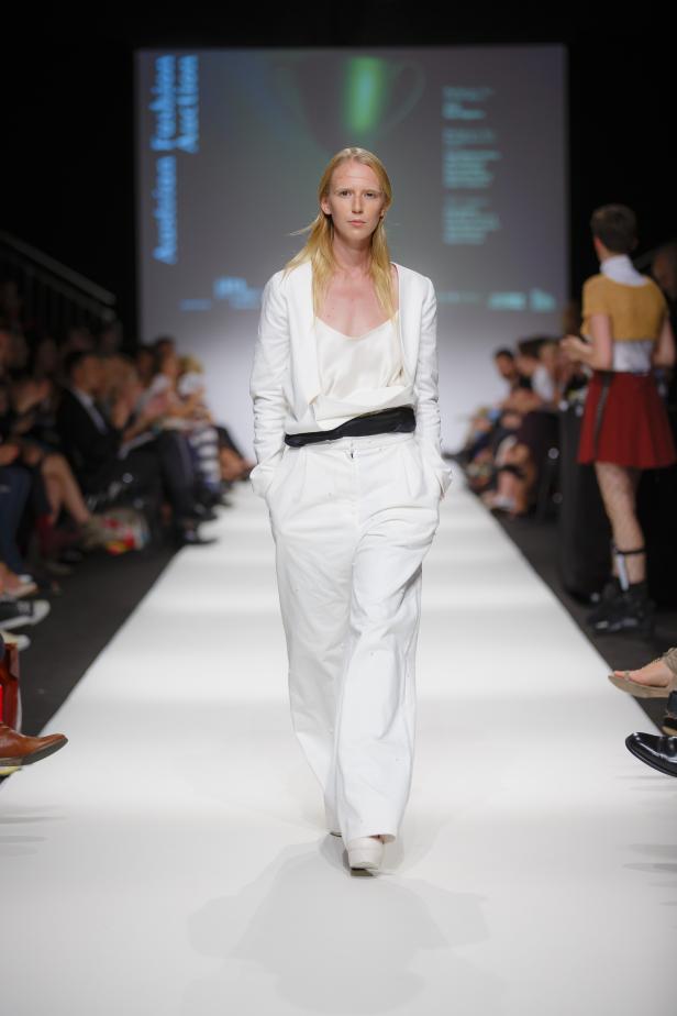 Eine blonde Person in einem weißen Hosenanzug auf einem Laufsteg.