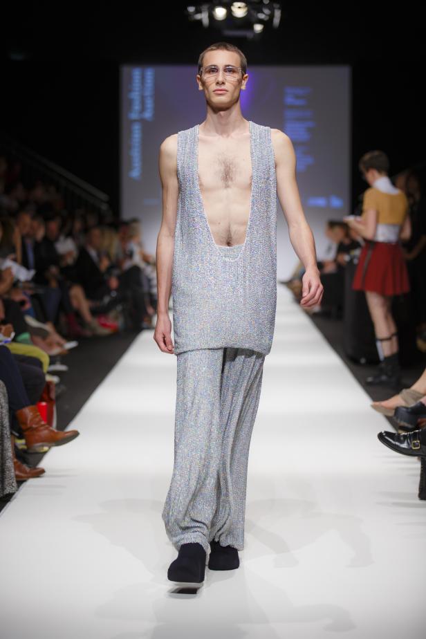 Ein Mann präsentiert ein glitzerndes, tief ausgeschnittenes Outfit auf einem Laufsteg.