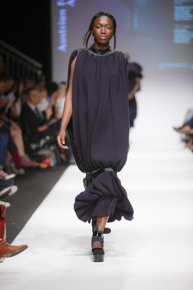 Eine dunkelhäutige Frau präsentiert ein voluminöses, dunkles Strickkleid auf einem Laufsteg.
