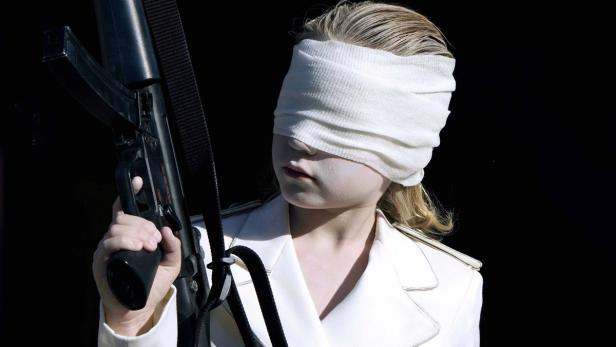 Ein Kind mit verbundenen Augen hält ein Gewehr in der Hand.