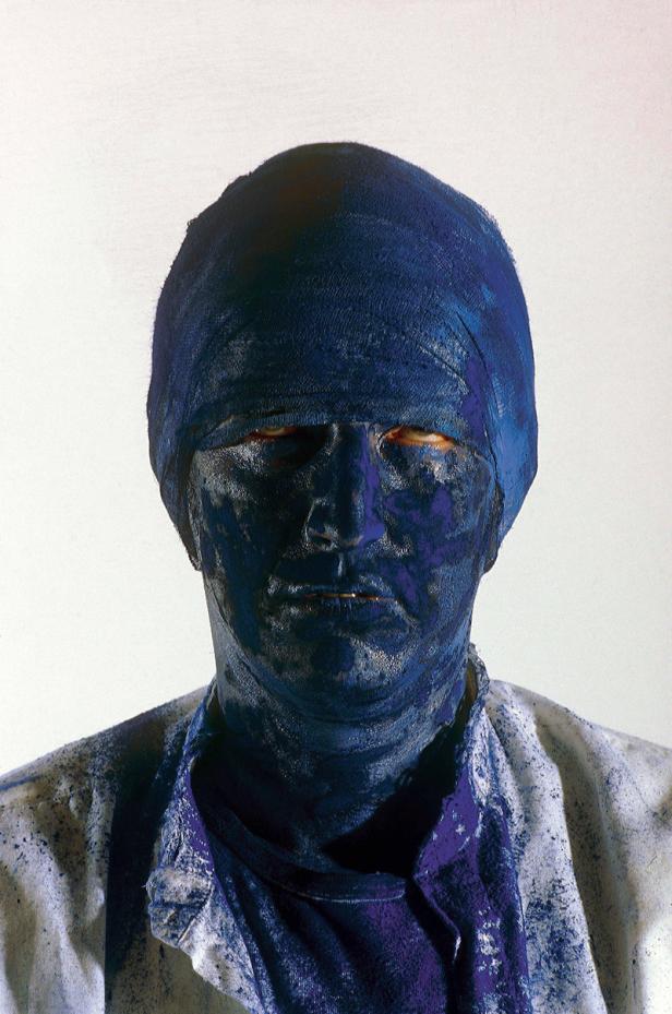 Das Gesicht eines Mannes ist mit blauer Farbe bedeckt, er trägt ein Tuch auf dem Kopf.