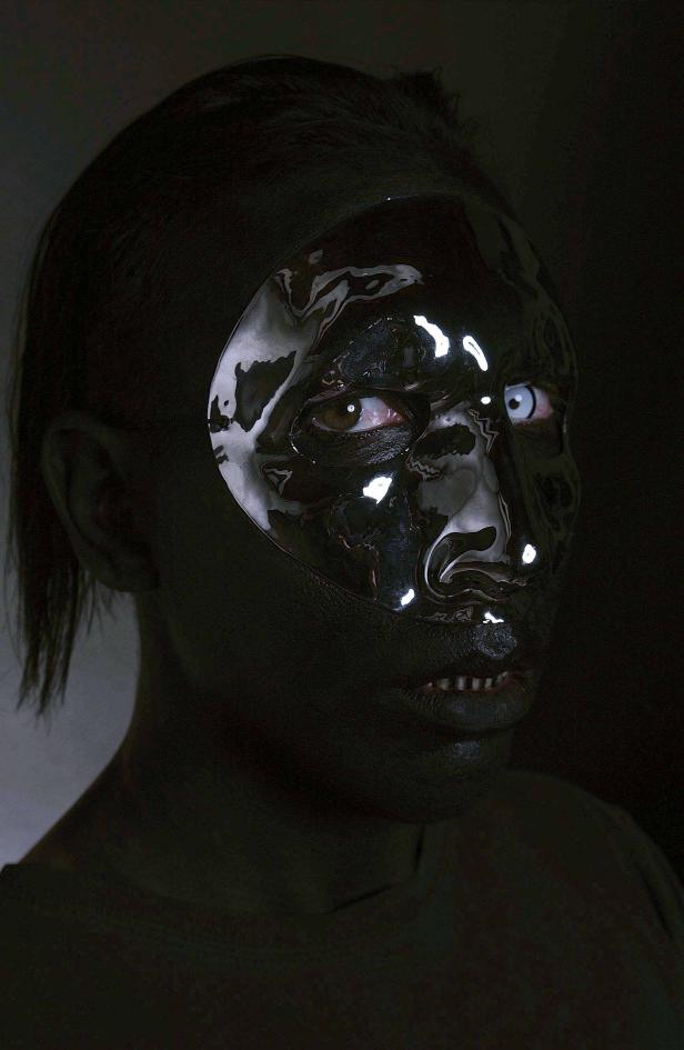 Eine Person mit schwarzer Farbe im Gesicht und einer reflektierenden Maske.