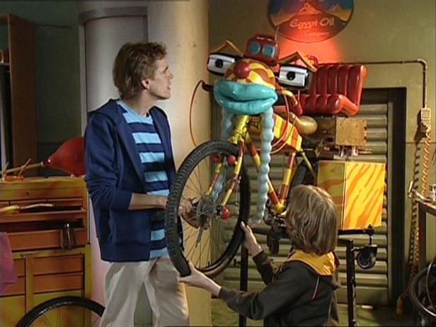 Zwei Personen reparieren ein ungewöhnliches, buntes Fahrrad in einer Werkstatt.