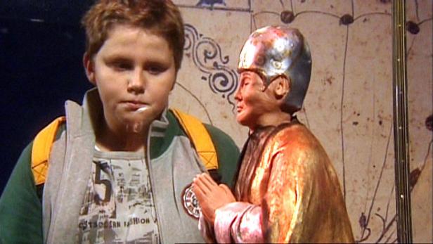 Ein Junge steht neben einer Statue mit gefalteten Händen.