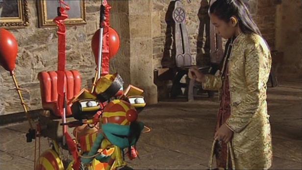 Ein Mädchen in traditioneller Kleidung steht vor einer bunten, mechanischen Puppe.