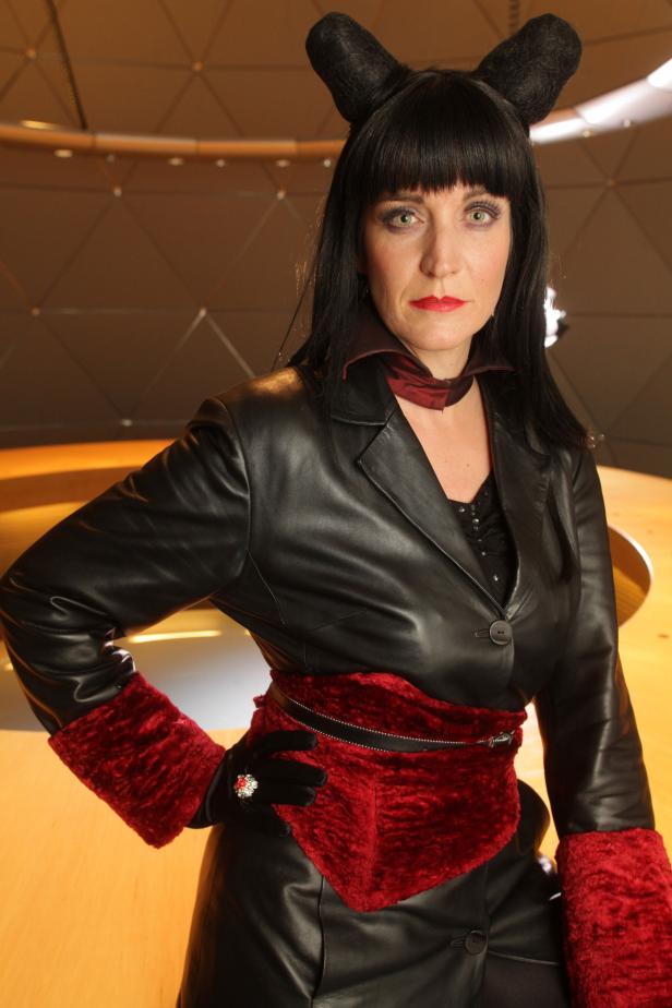 Eine Frau mit schwarzen Haaren und Katzenohren in einem schwarzen Lederoutfit mit roten Akzenten.