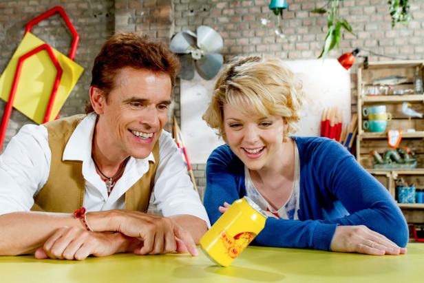 Ein Mann und eine Frau betrachten lächelnd eine gelbe Getränkedose auf einem Tisch.