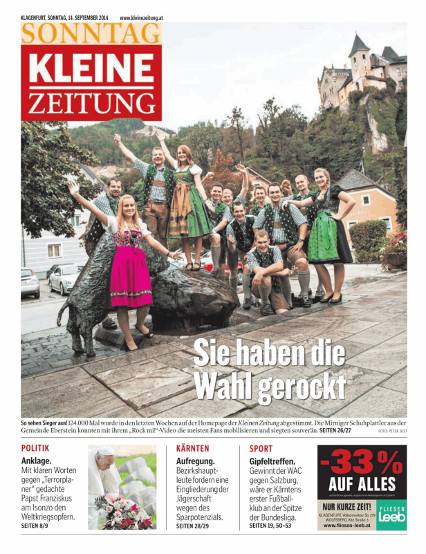 Eine Gruppe von Personen in Tracht posiert vor einer Statue und einem Gebäude.
