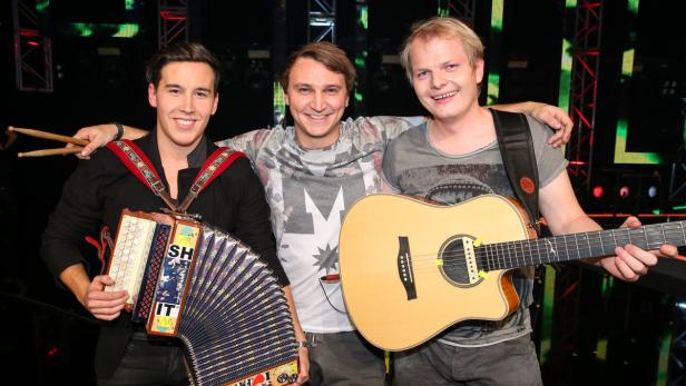 Drei Musiker posieren mit Akkordeon und Gitarre vor einer Bühne.