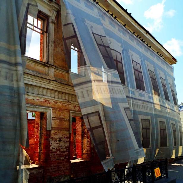 Ein verfallendes Gebäude ist mit einer Plane verdeckt, die eine Fassade zeigt.