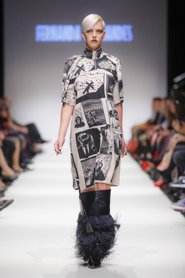 Eine Frau mit blonden Haaren präsentiert ein Kleid mit Comic-Motiven und Stiefel mit Federn auf dem Laufsteg.