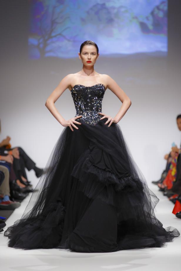 Eine Frau präsentiert ein schwarzes, trägerloses Abendkleid auf einem Laufsteg.