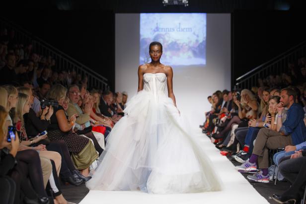 Eine dunkelhäutige Frau in einem weißen Kleid auf dem Laufsteg bei einer Modenschau von Dennis Diem.