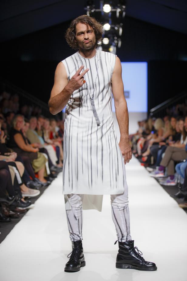 Ein Mann mit langen Haaren auf einem Laufsteg, der ein gestreiftes Outfit und Stiefel trägt.