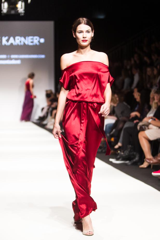 Eine Frau in einem roten Seidenoverall auf einem Laufsteg.