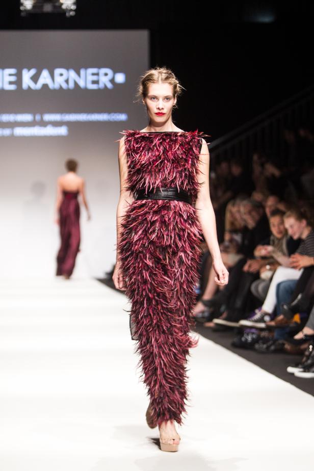 Eine Frau präsentiert ein burgunderrotes Federkleid auf dem Laufsteg.