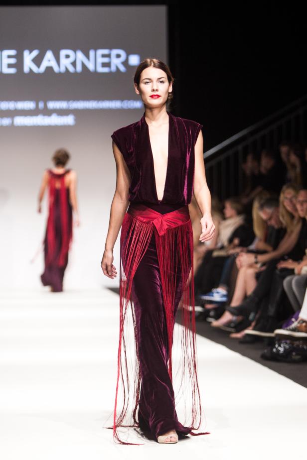 Eine Frau in einem langen, burgunderroten Kleid mit Fransen auf einem Laufsteg.
