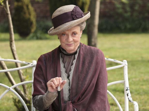 Maggie Smith als Violet Crawley in „Downton Abbey“ sitzt auf einer Bank.