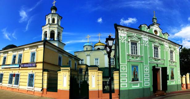 Mehrere farbenfrohe Gebäude mit orthodoxen Kuppeln und Kreuzen unter einem blauen Himmel.